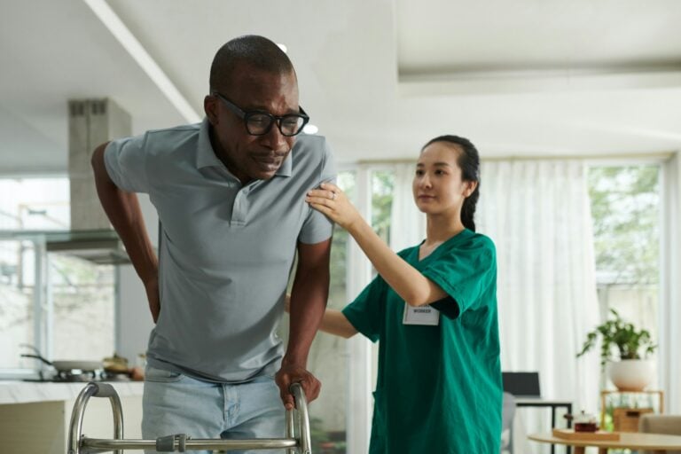 Caregiver assisting elderly man with walker.