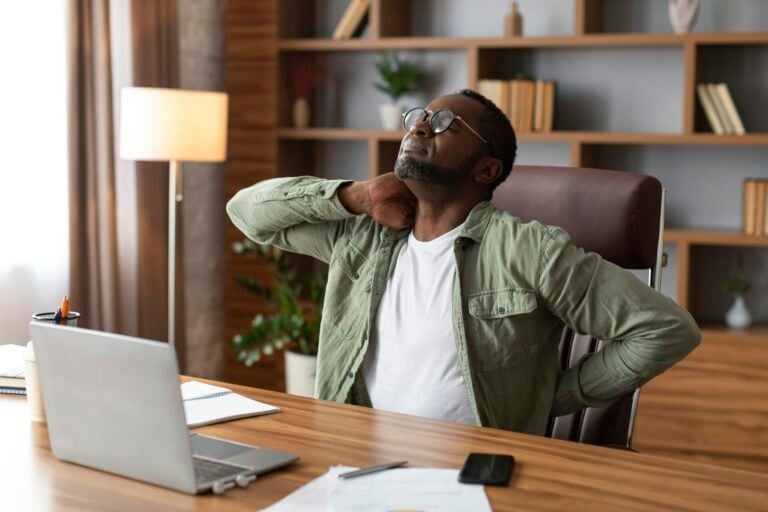 Man stretching at his desk, neck pain.
